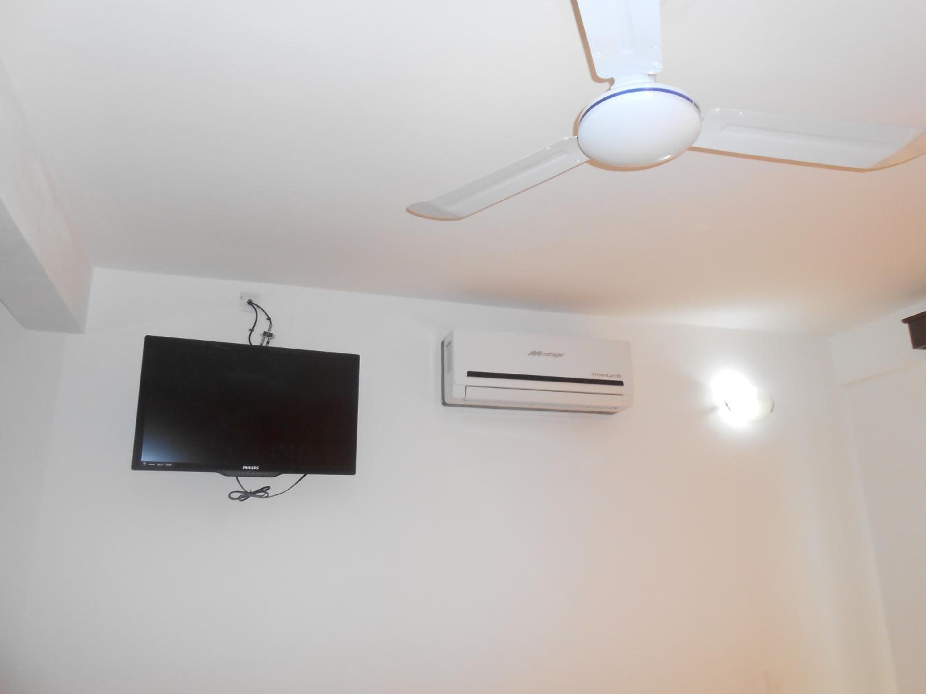 A ceiling fan, a mounted television, and an air conditioning unit in a room.
