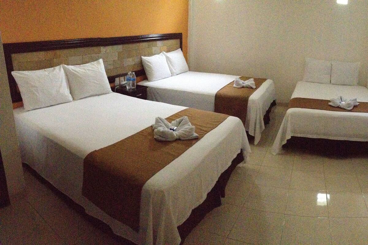 A hotel room with two beds, each with white linens and brown headboards. There are two bedside tables with water bottles on them.