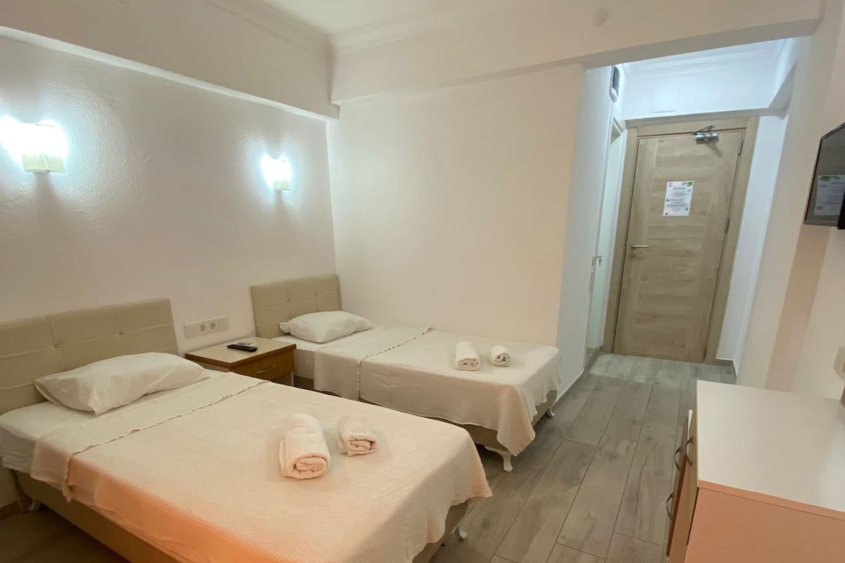 A hotel room with two single beds, a wooden floor, a desk, and a door with a sign.