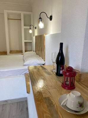 A hotel room with a wooden bed, a bedside table with a wine bottle, glasses, a red lantern, and a cup on a saucer. - Hotel Unver (Marmaris)