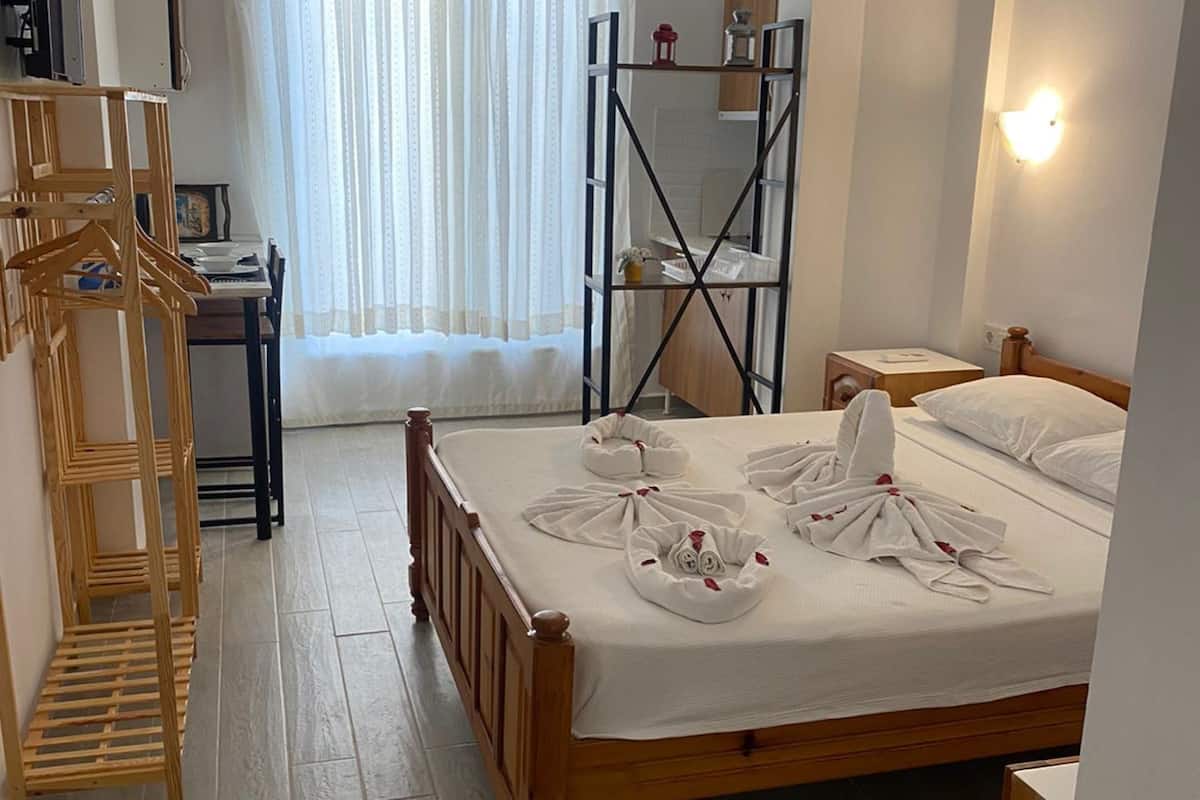 A hotel room with a wooden bed, a desk, a chair, a wardrobe, and a window with curtains.