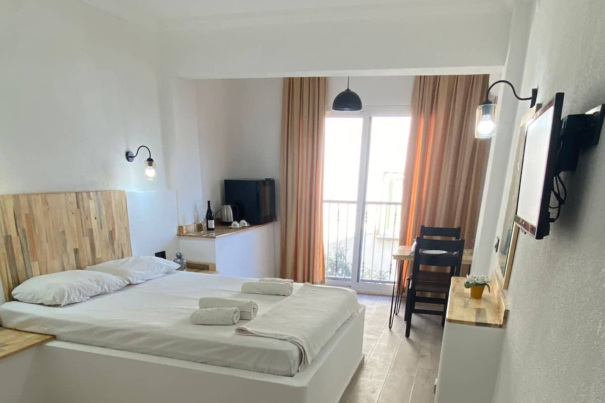 A modern hotel room with a large bed, a desk, a TV, and a balcony with curtains.