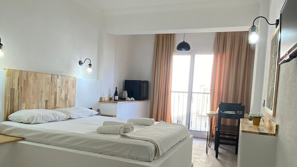 Una habitación de hotel moderna con una cama grande, un escritorio pequeño, televisión y un balcón con cortinas.