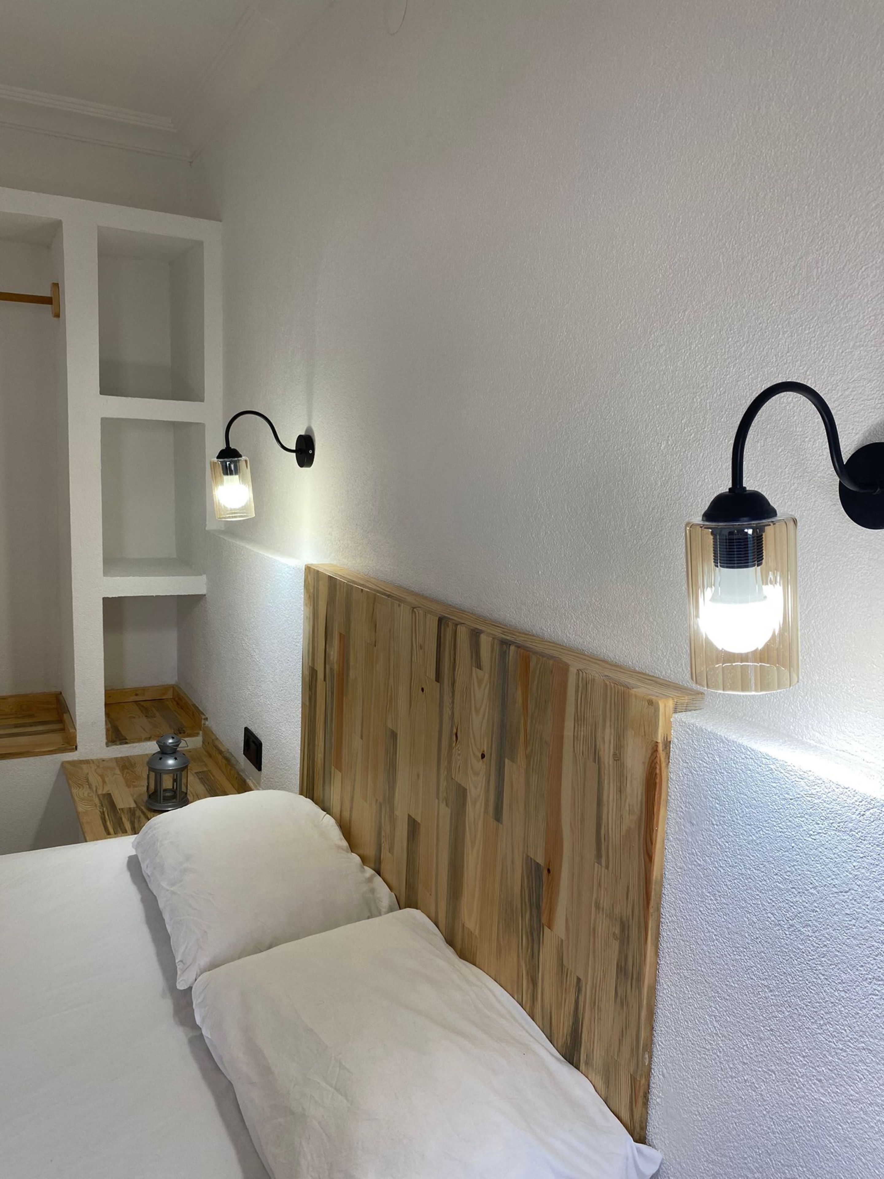 Una camera da letto con una testiera in legno, un letto con biancheria da letto bianca, un comodino con una lanterna e due luci a parete.