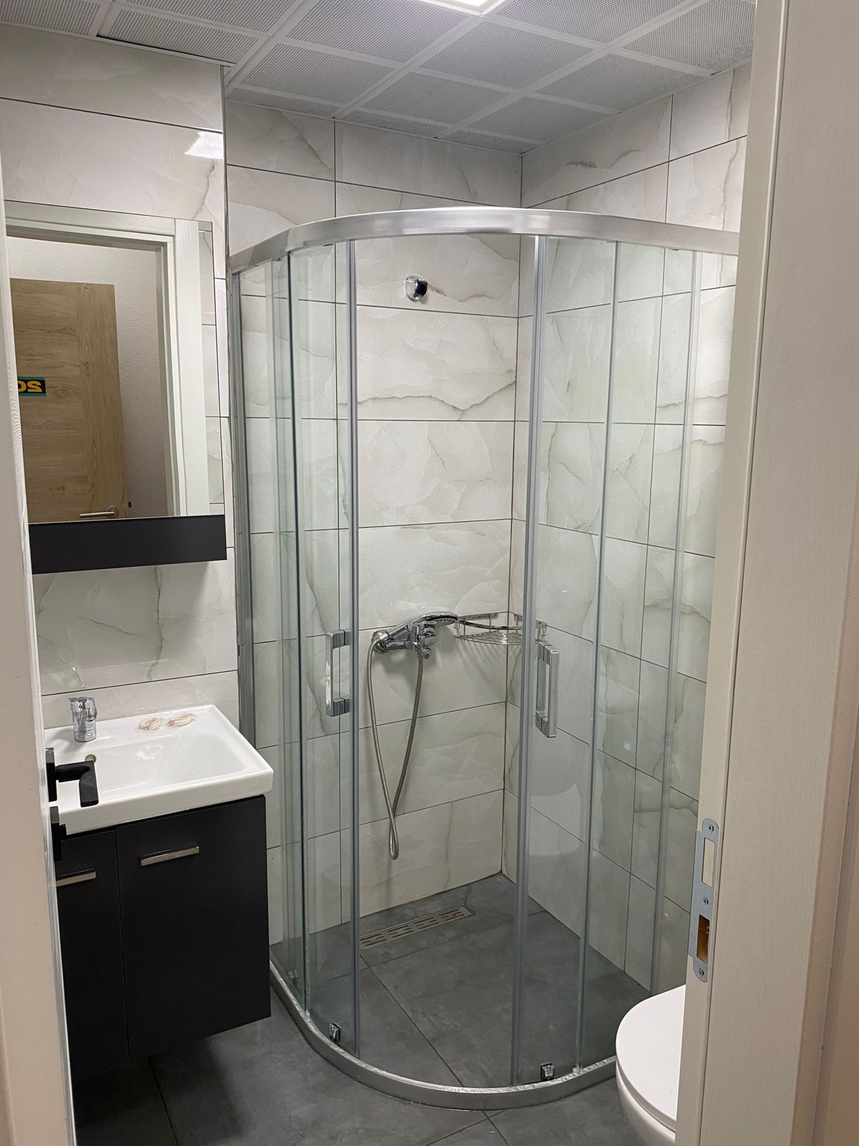 A modern bathroom with a glass-enclosed shower, a white sink, and a mirror above the sink.