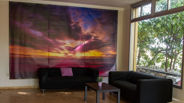 A room with a large abstract painting, a black sofa, a small table, and a view of trees through a window. - Quintasol (Malgrat de Mar)