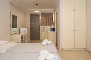 Quarto de hotel com cama, secretária, cadeira, cozinha compacta e guarda-roupa.