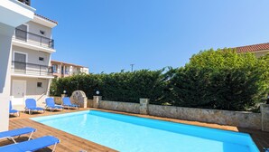 A swimming pool with blue lounge chairs, a stone wall, and a building with balconies. - Karras Livin (Zakynthos)