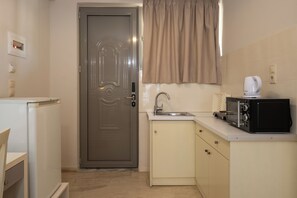 A compact kitchen with a refrigerator, a microwave, a sink, and a door with a handle. - Karras Livin (Zakynthos)