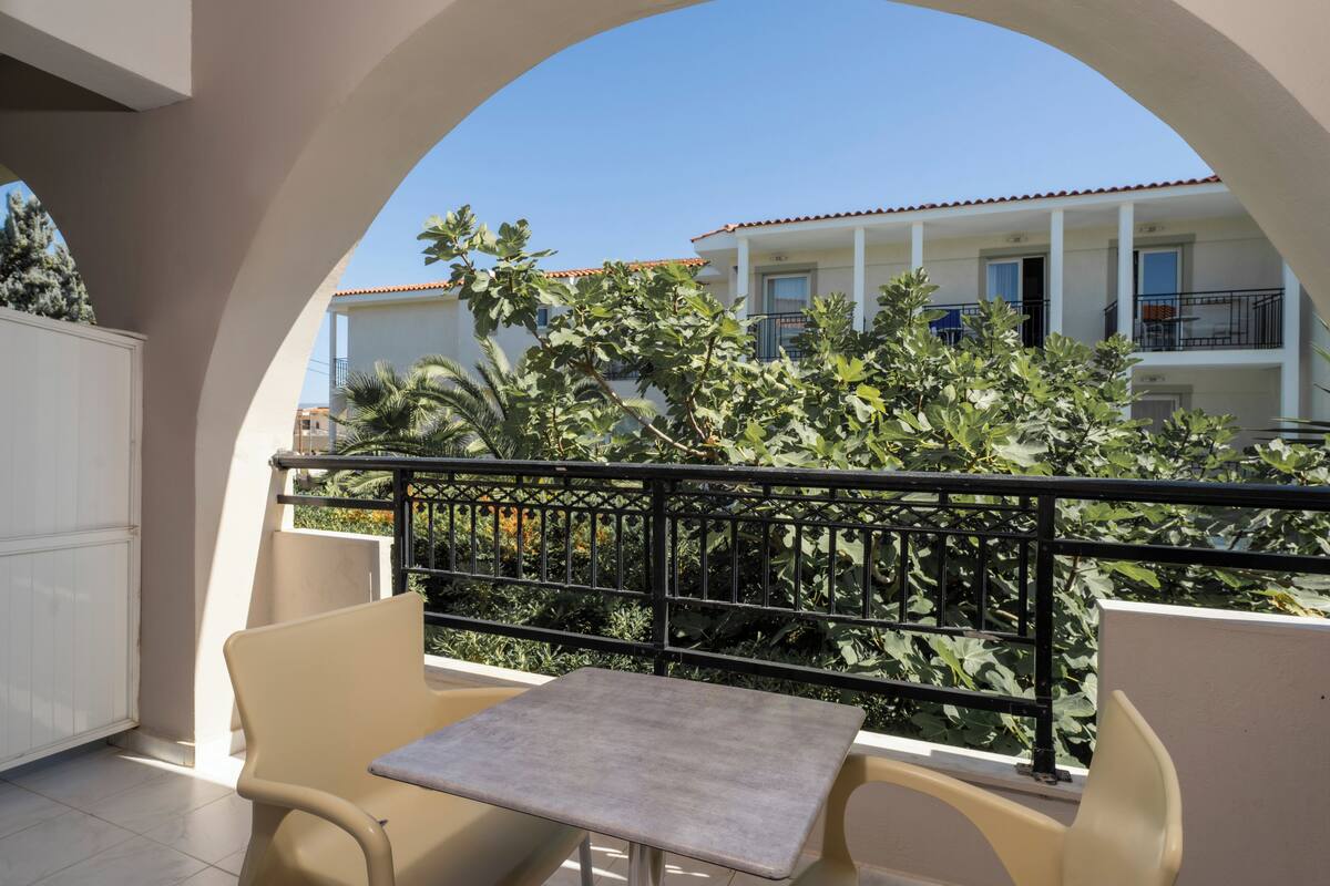 A balcony with a table and chairs, a railing, and a view of a building with balconies.