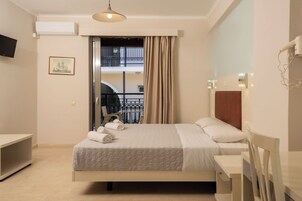 Quarto de hotel com cama, escrivaninha, cadeira, televisão e varanda com guarda-corpo.