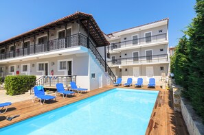 A hotel with a swimming pool, blue lounge chairs, and a wooden deck. - Karras Livin (Zakynthos)