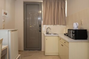 A compact kitchen with a refrigerator, a microwave, a sink, and a door with a handle. - Karras Livin (Zakynthos)