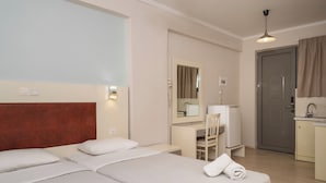 A hotel room with two beds, a desk, a chair, a mirror, a door, and a kitchenette. - Karras Livin (Zakynthos)