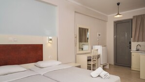 A hotel room with two beds, a desk, a chair, a mirror, a door, and a kitchenette. - Karras Livin (Zakynthos)