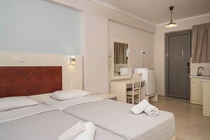 A hotel room with two beds, a desk, a chair, a mirror, a door, and a kitchenette. - Karras Livin (Zakynthos)
