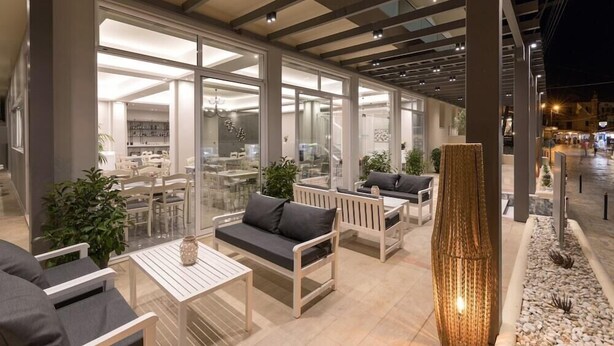 Un área de estar interior con mesas y sillas, ventanas amplias y una planta decorativa.