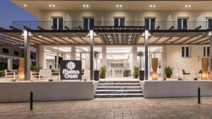 Una entrada moderna de hotel con un área exterior cubierta, un letrero que dice "Mina Oasis" y una escalera que conduce a la entrada.