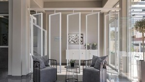 Un interior moderno con una zona de estar que incluye dos sofás grises y una pequeña mesa redonda, separadas por un panel blanco con diseño de malla.