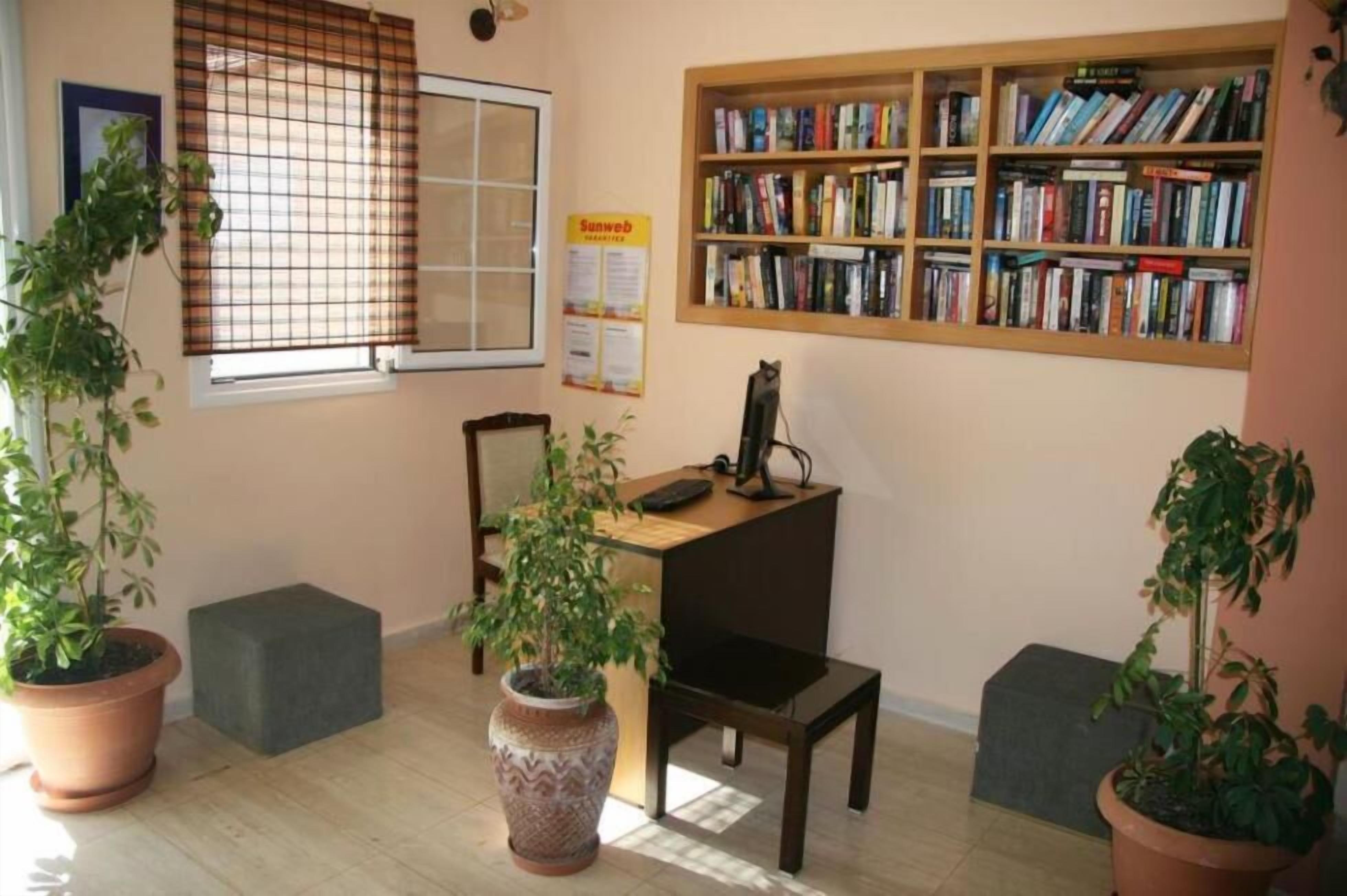Una stanza con una libreria, una scrivania, una sedia e piante in vaso.
