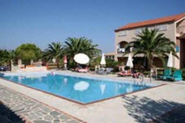 A swimming pool with lounge chairs and palm trees, surrounded by a building with a tiled roof. - Daniel Hotel (Zakynthos)