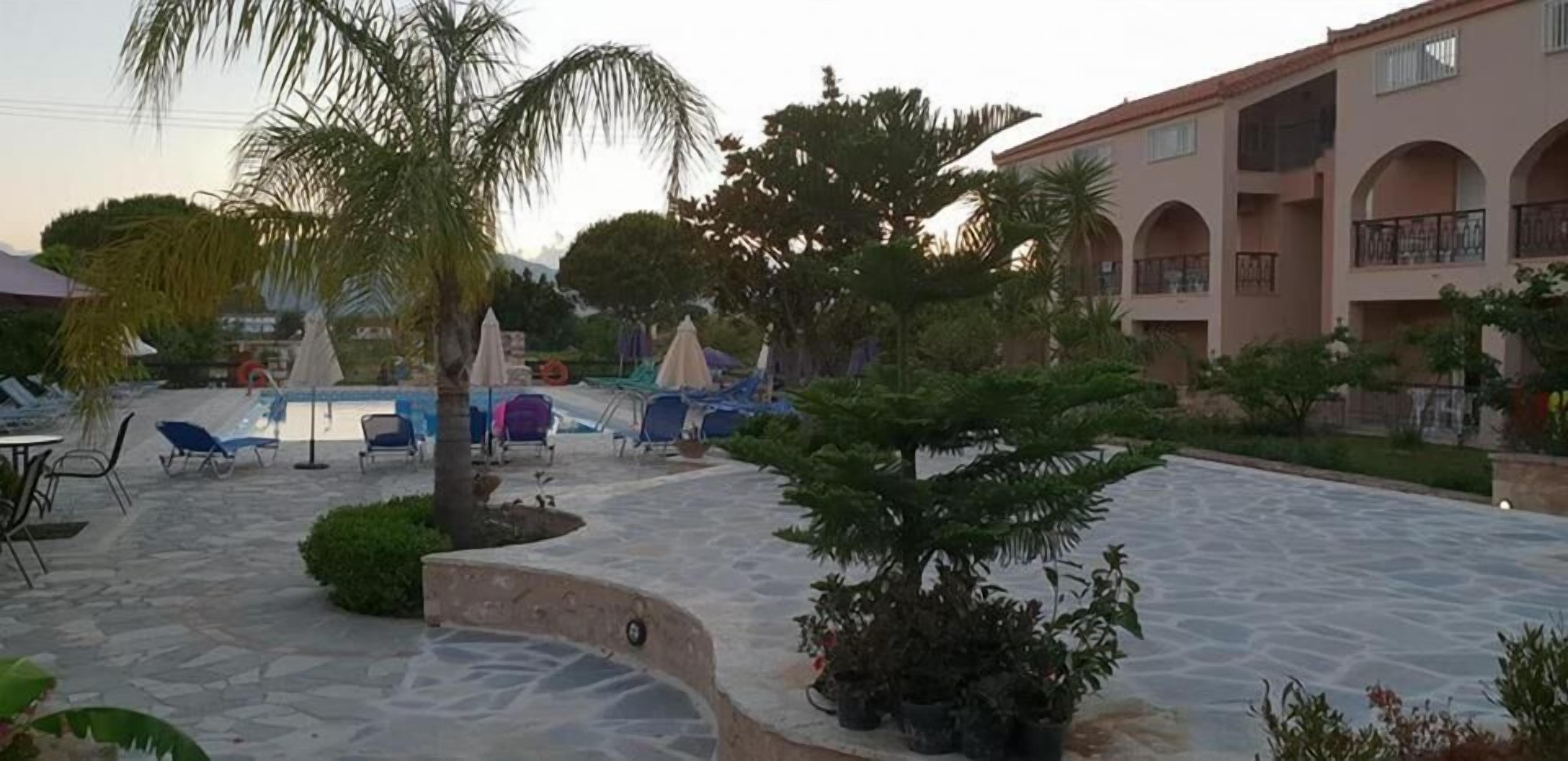 A courtyard with stone flooring, lounge chairs, umbrellas, and potted plants.