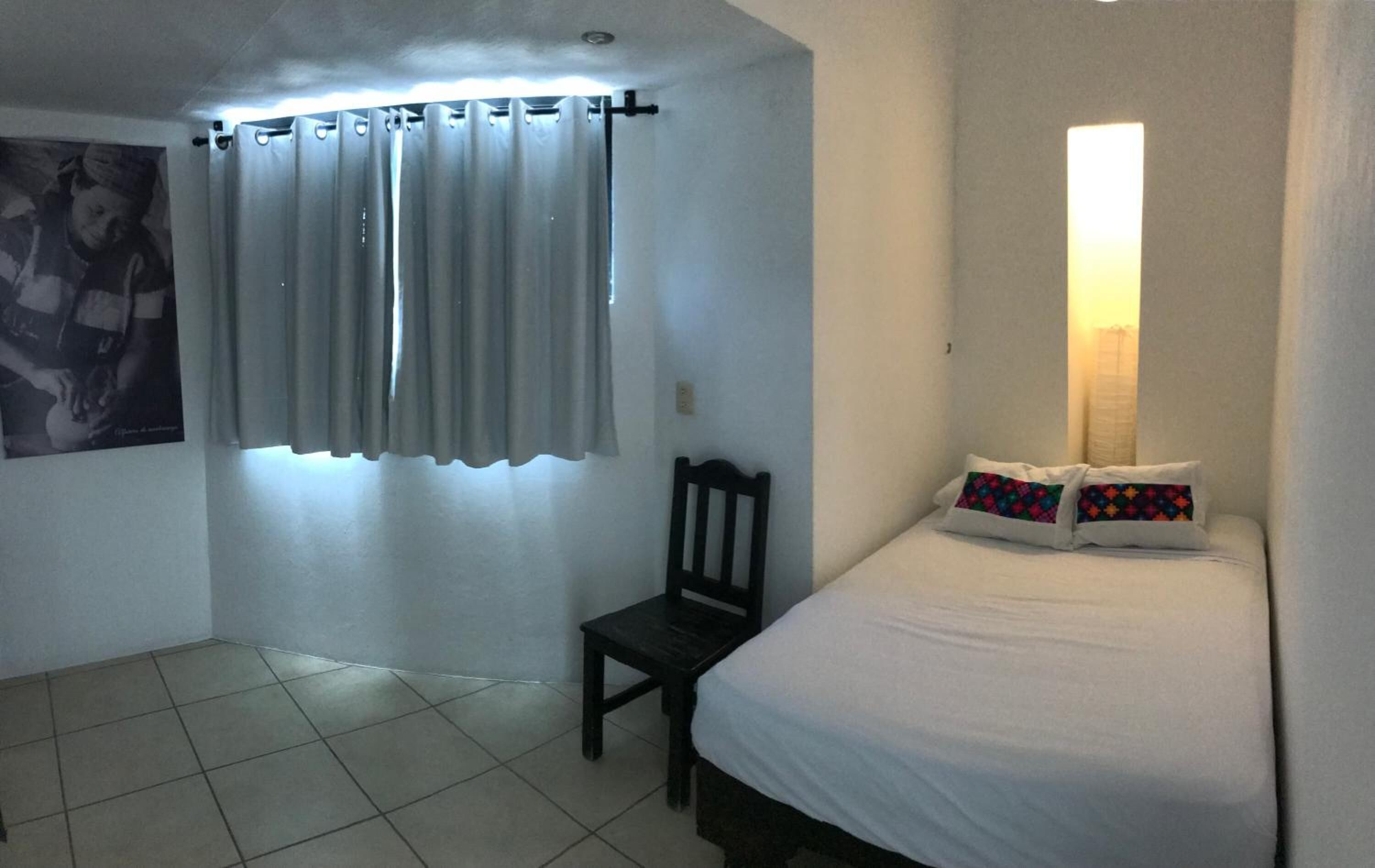Una habitación pequeña y limpia con cama, una silla y ventana con cortinas.
