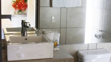 Un baño moderno con un lavabo grande, inodoro y bidé. Hay un perchero sobre el inodoro y una pequeña planta en la encimera.