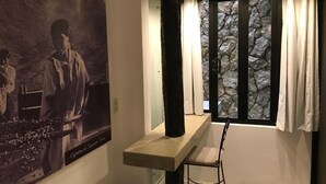 A room with a stone wall, a window with curtains, a wooden table, and a chair. - Hotel Maya Rue (Palenque)
