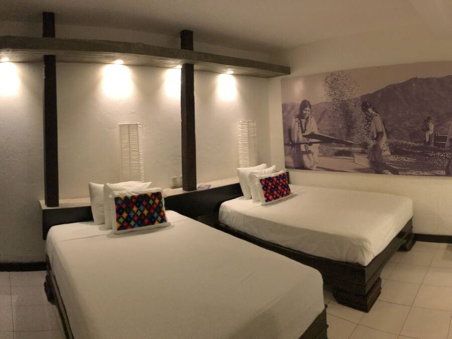 Quarto de hotel com duas camas, uma televisão de parede grande e uma pintura de uma cena histórica.