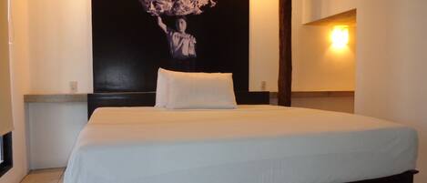 A neatly made bed in a hotel room with a dark headboard, a wall-mounted light, and a large floral artwork above the bed.