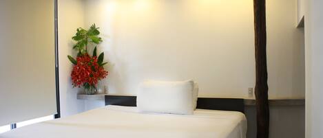 Una habitación de hotel con una cama, una mesita de noche, un jarrón con flores rojas y un pilar de madera.