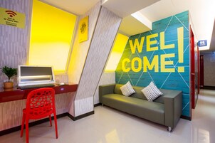 Een receptiegedeelte met een laptop op een bureau, een rode stoel, een groene bank met kussens en een muur met daarop de tekst 'WELCOME'.