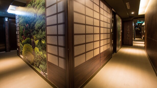 Un pasillo con un muro decorado en estilo tradicional japonés que representa una escena natural.