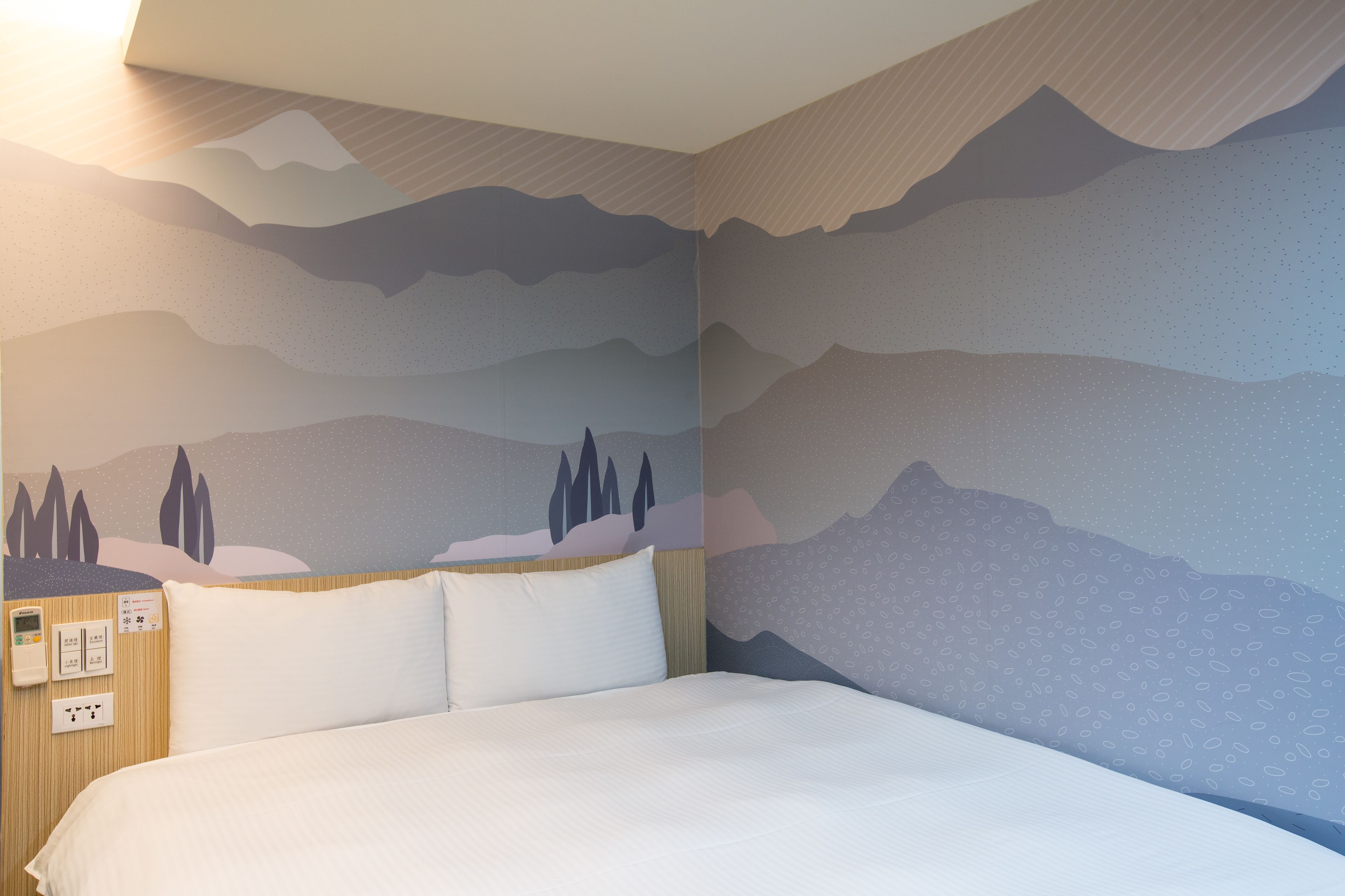 Ein Hotelzimmer mit einem Bett, einem wandmontierten Thermostat und einer Bedienkonsole.