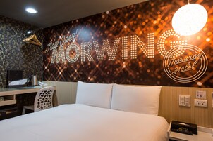 Een hotelkamer met een bed, een bureau en een muur met verlichte tekst.