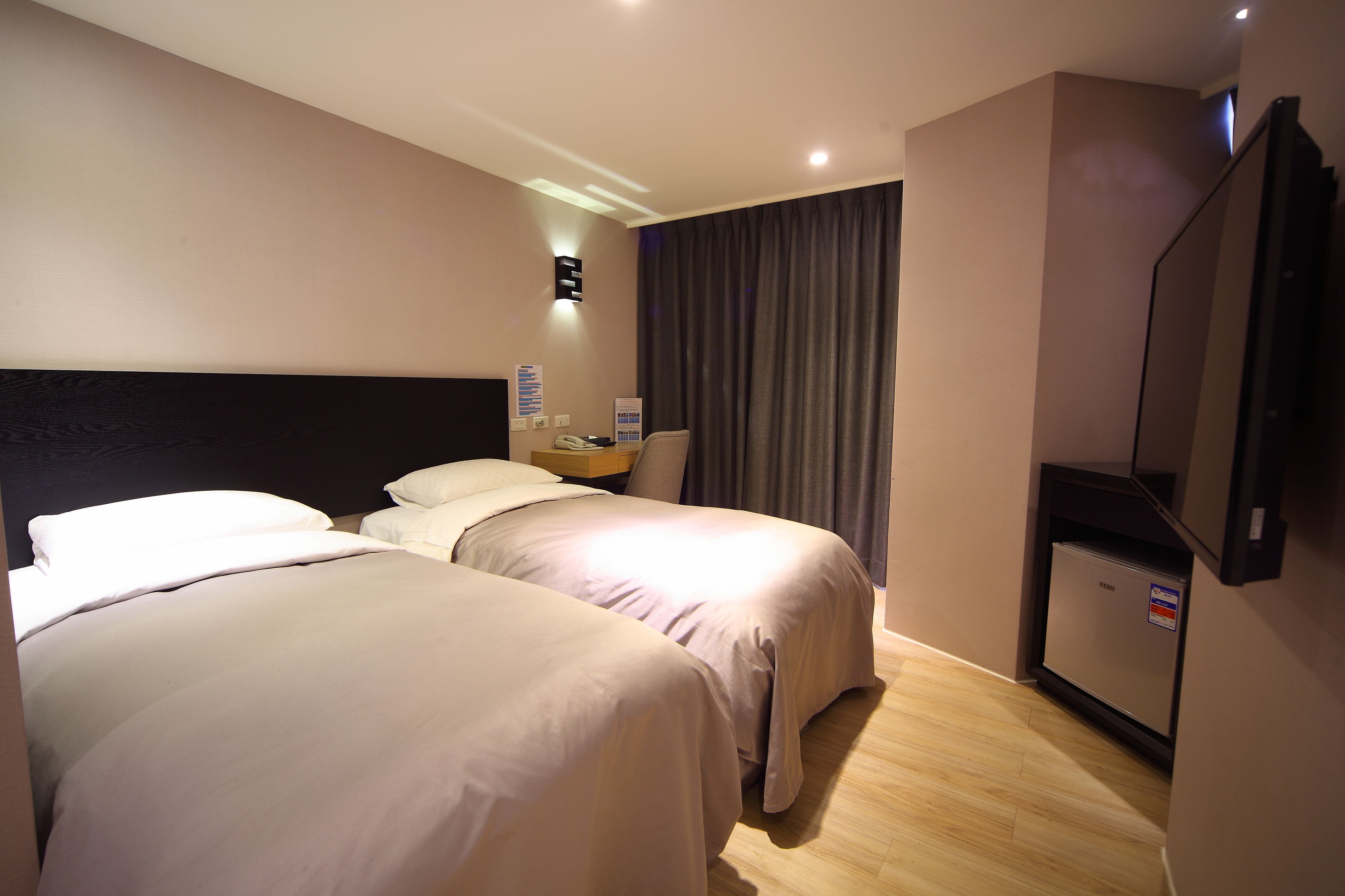 Een hotelkamer met twee bedden, een bureau met telefoon, een flatscreen televisie en een wandlamp.