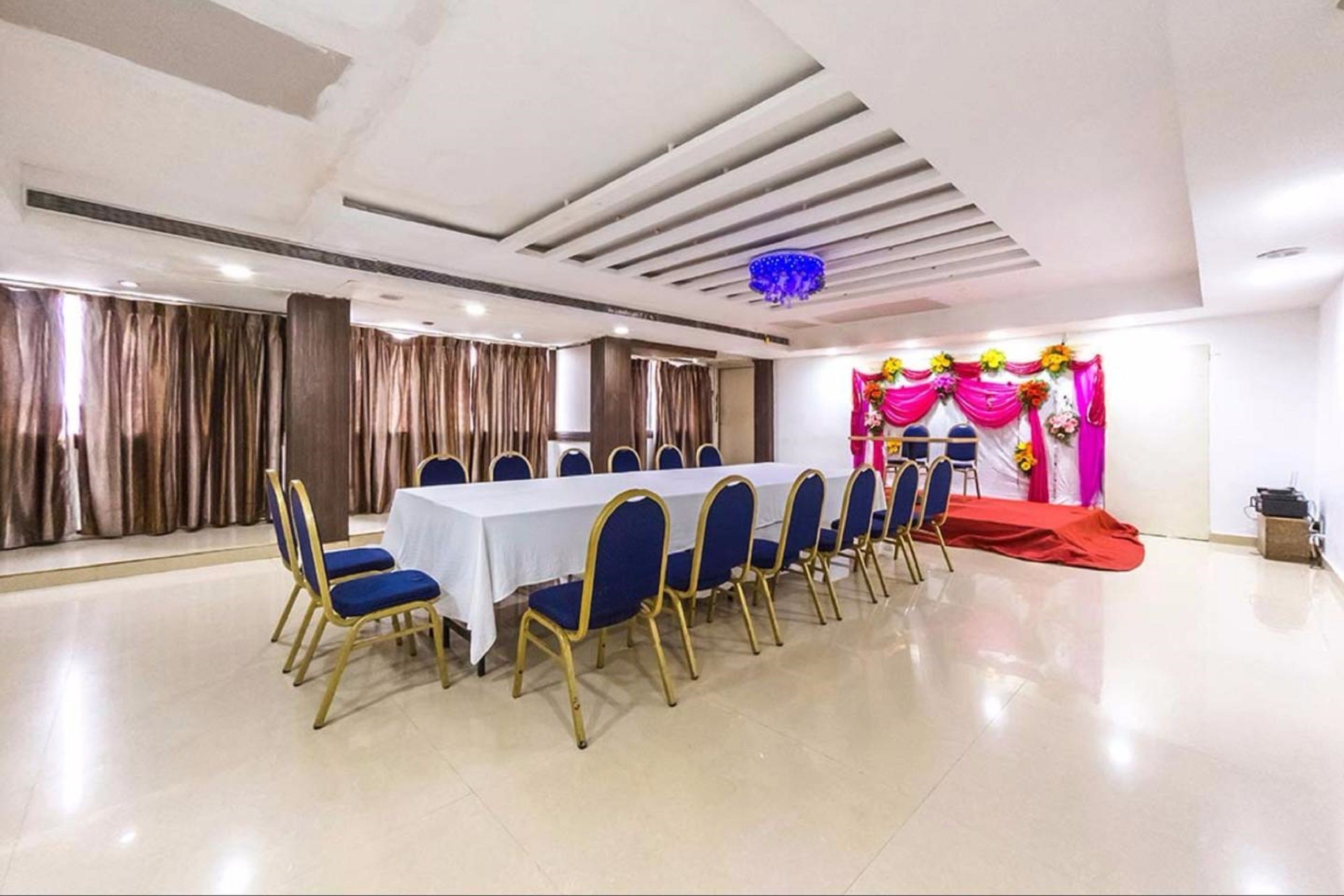 Un salón de conferencias con una larga mesa y sillas azules, un escenario con decoraciones coloridas y una alfombra roja.