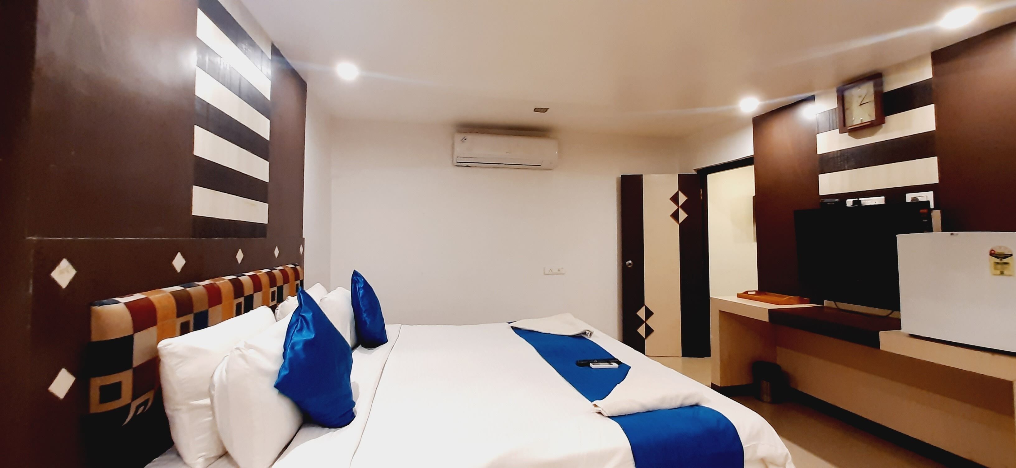 A hotel room with a bed, a desk, a TV, and an air conditioning unit.