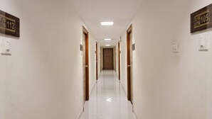 A long, narrow hallway with doors on both sides, numbered signs above each door, and a clean, tiled floor. - Hotel Kosala (Vijayawada)