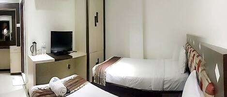 Habitación de hotel con dos camas, un escritorio y un televisor, y un equipo de aire acondicionado.
