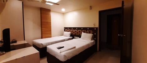 Habitación de hotel con dos camas individuales, un escritorio con silla, ventilador de techo y una puerta.