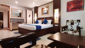 A hotel room with a bed, bedside table, chair, and a small table. - Hotel Kosala (Vijayawada)