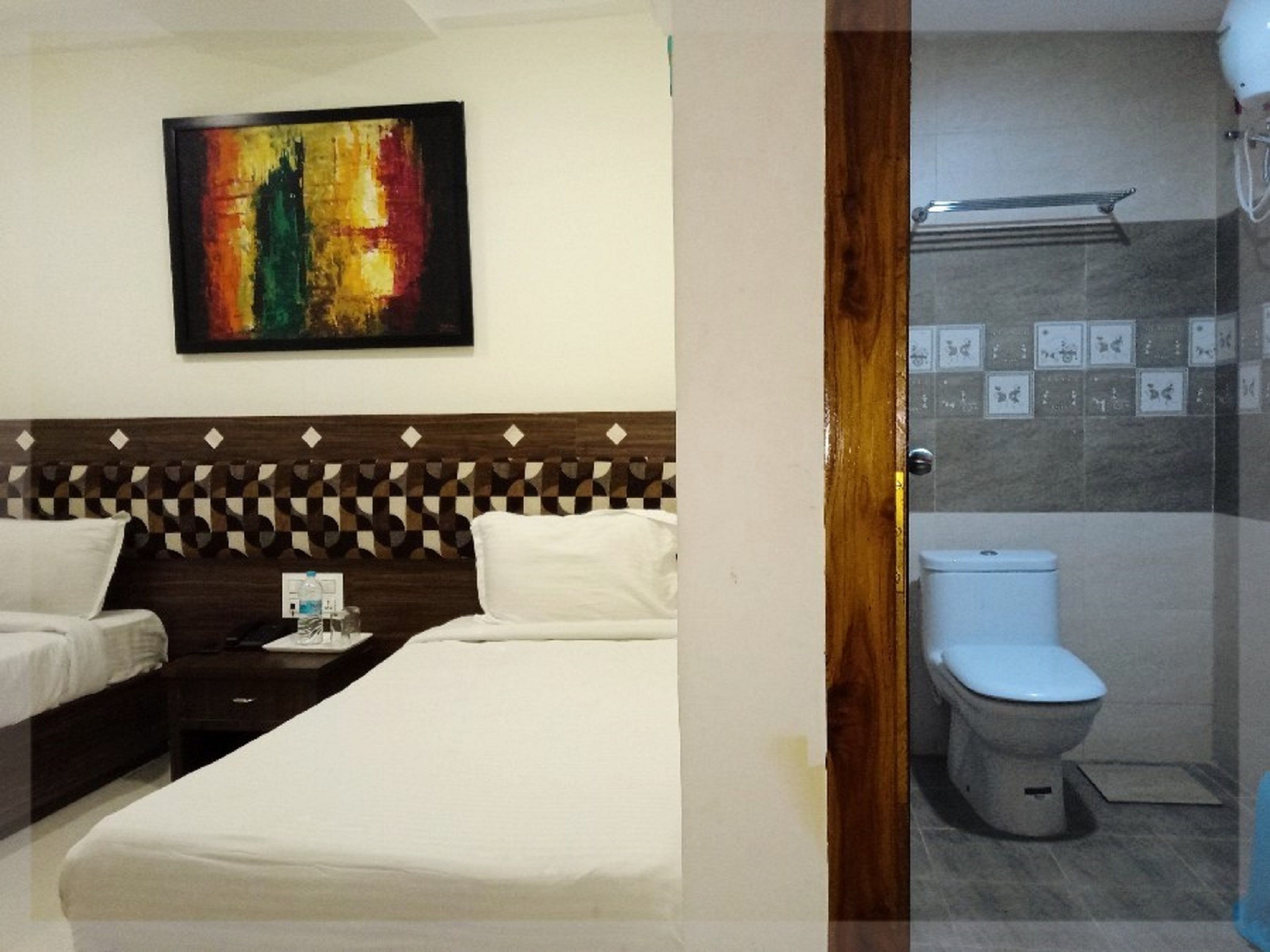 A hotel room with a bed, a nightstand, a painting on the wall, and a bathroom with a toilet and shower.