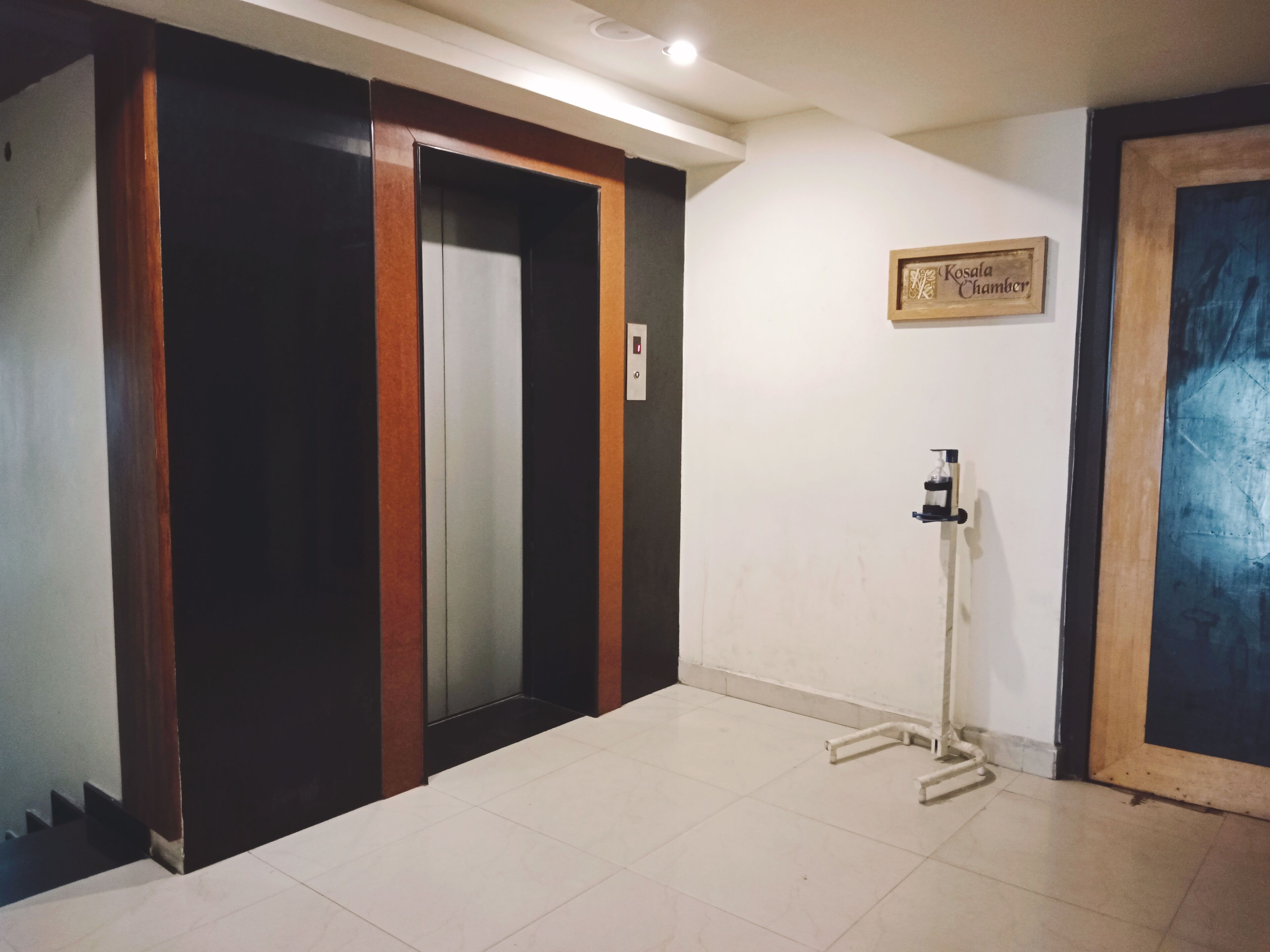 Ascensore con un cartello sopra, un erogatore di acqua e una porta con un cartello che recita "Kosala Chamber".