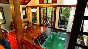 A spacious indoor swimming pool with a wooden deck and a view of lush greenery outside. - Vythiri Resort (Vythiri)