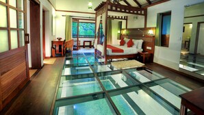 A room with a glass floor, a bed with red pillows, and a wooden ceiling structure. - Vythiri Resort (Vythiri)
