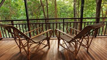 A wooden deck with wicker chairs and a view of dense forest.