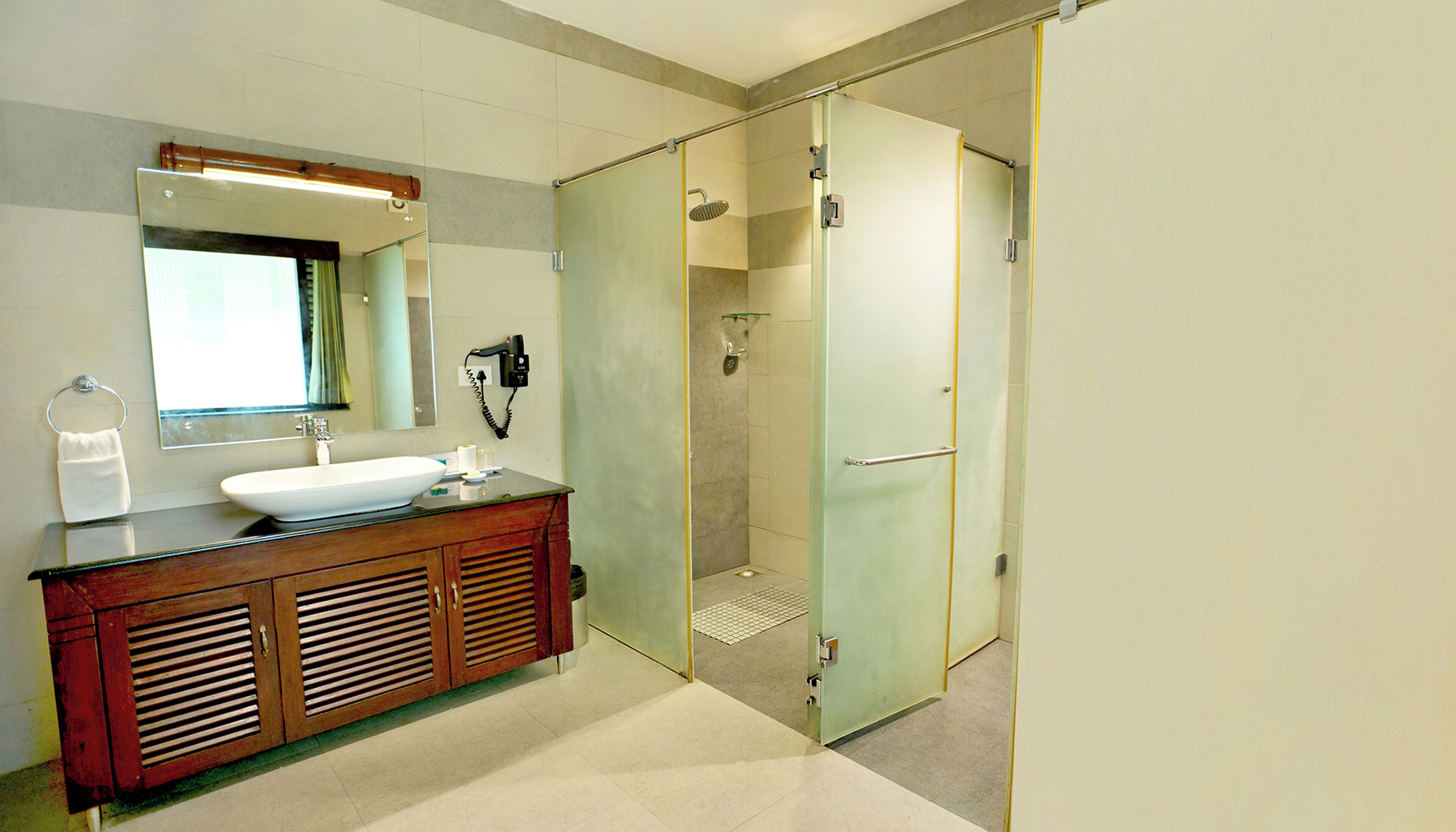 Een badkamer met een houten wastafelmeubel, een grote spiegel, een wastafel en een douche met glazen wanden.
