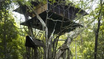 A treehouse structure built into a forested area with multiple levels and a metal staircase.